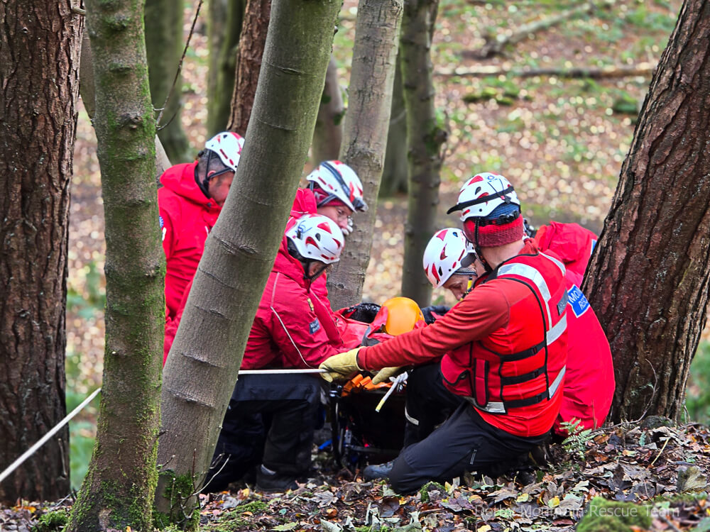 Team members in helmets working with ropes around a casualty on a steep wooded slope