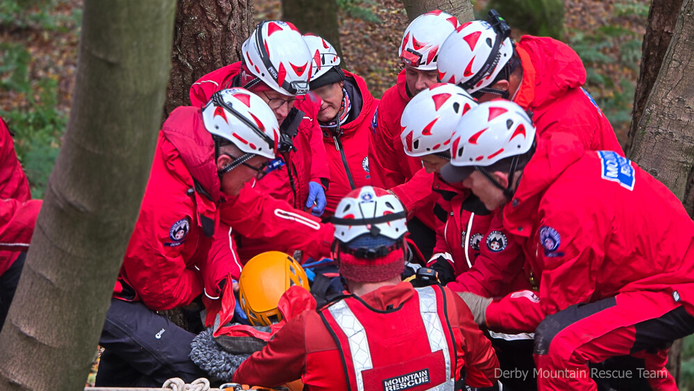 Team members in helmets working closely around a casualty on steep wooded ground